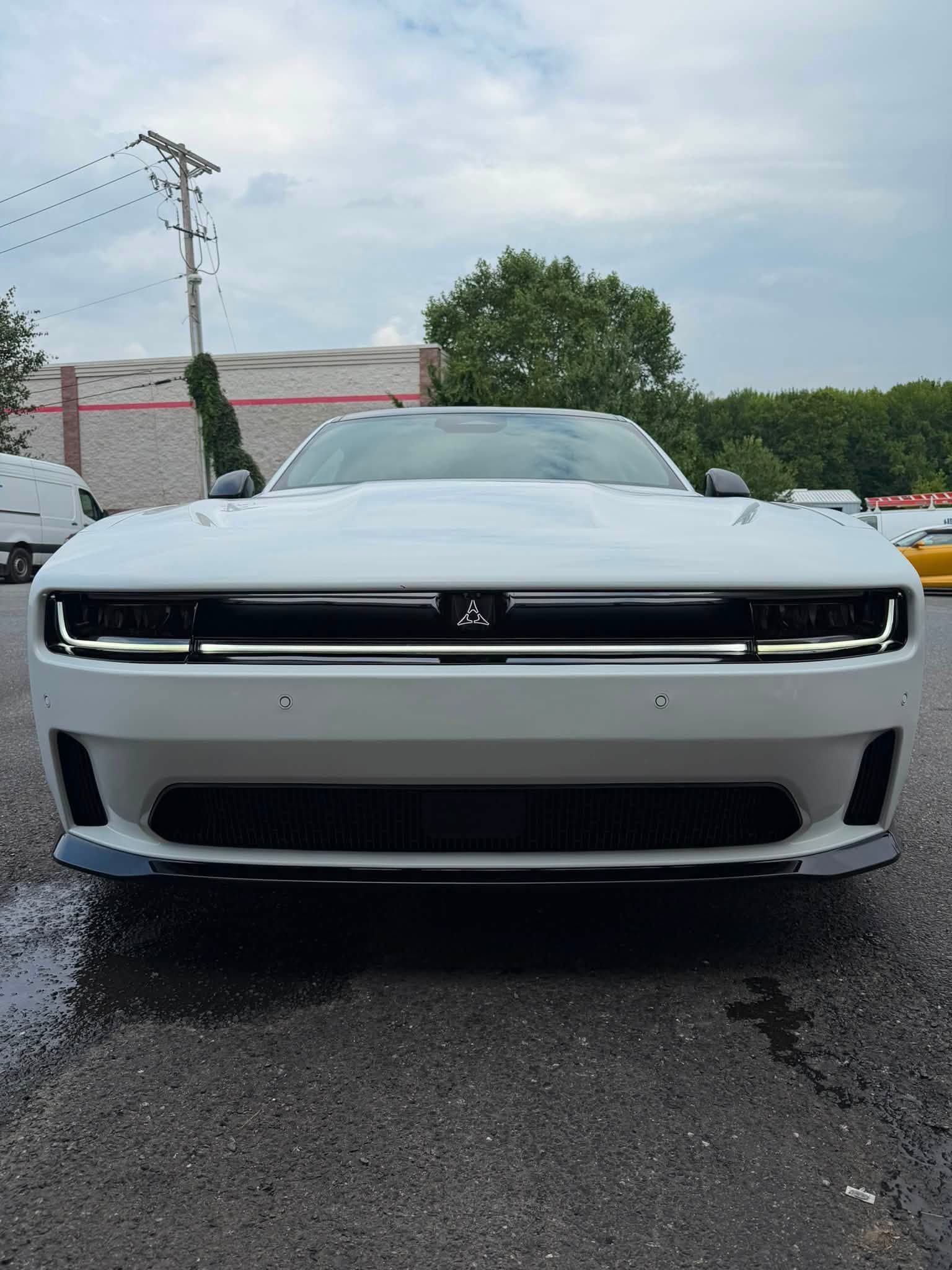 White Dodge Challenger viewed from the front in a wet parking lot under an overcast sky