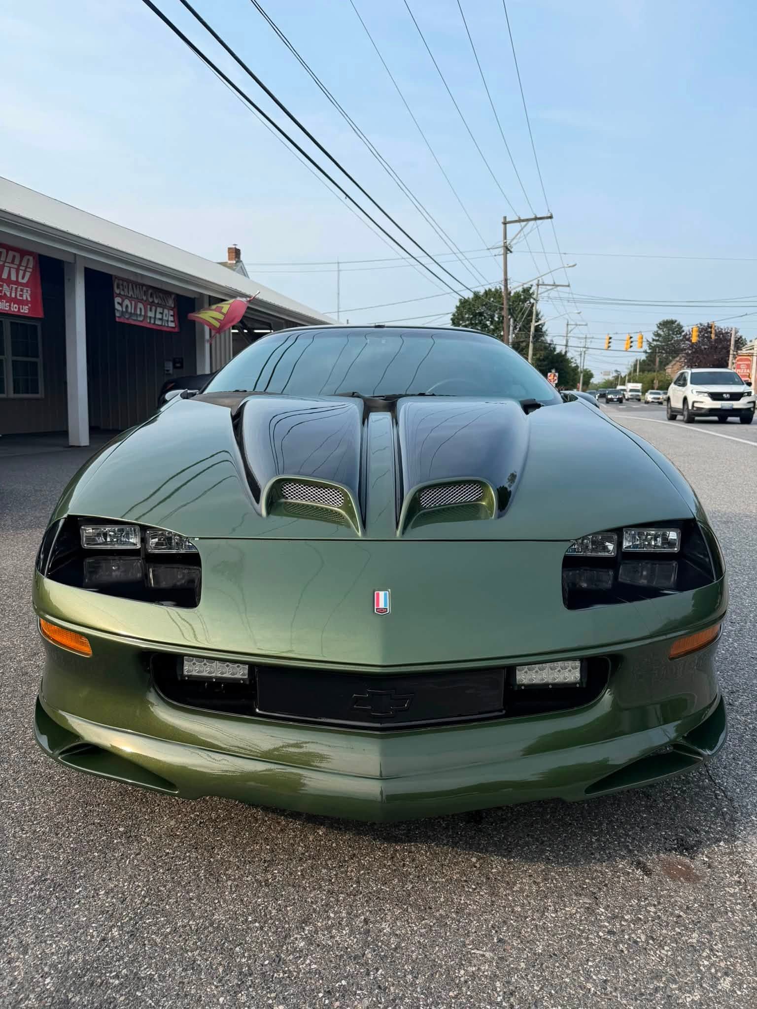 Green sports car parked on a street, front view with hood vents and tinted headlights.