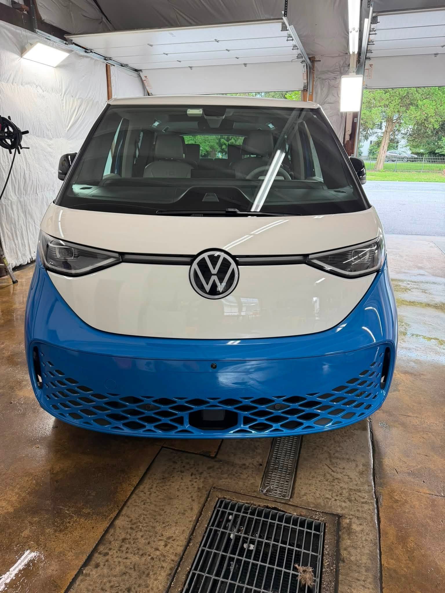 Blue and white Volkswagen van parked in a covered driveway, front view.