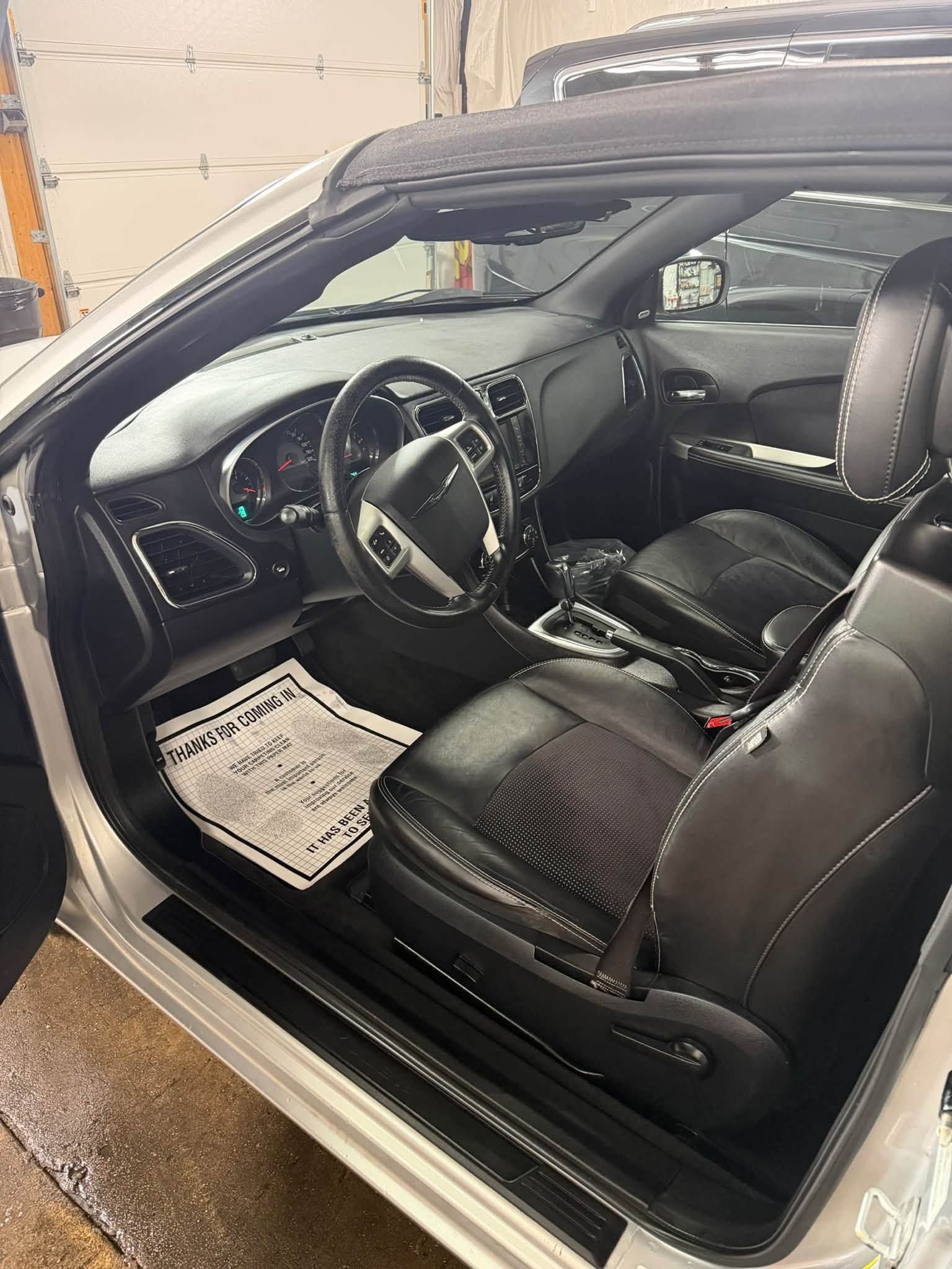 Black leather sports car interior with steering wheel, dashboard, and open driver’s door