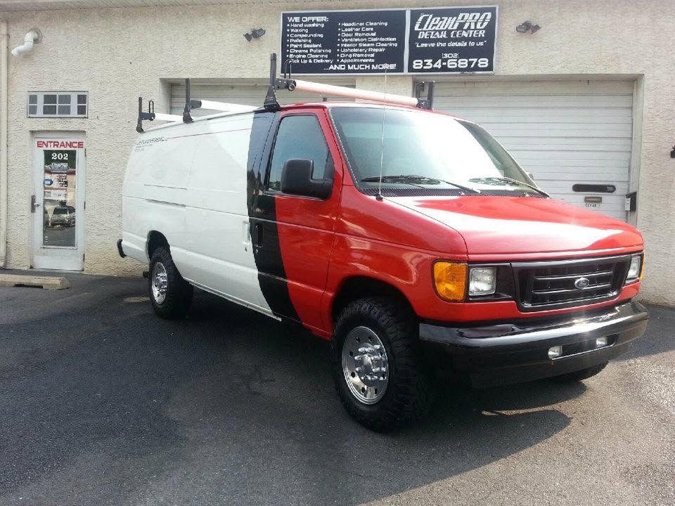 Red and white utility van parked outside a garage on a paved lot