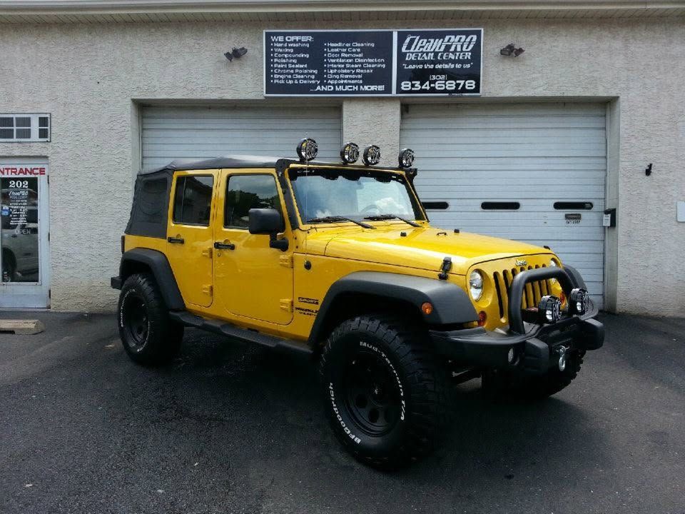Yellow lifted Jeep Wrangler parked outside a shop garage door