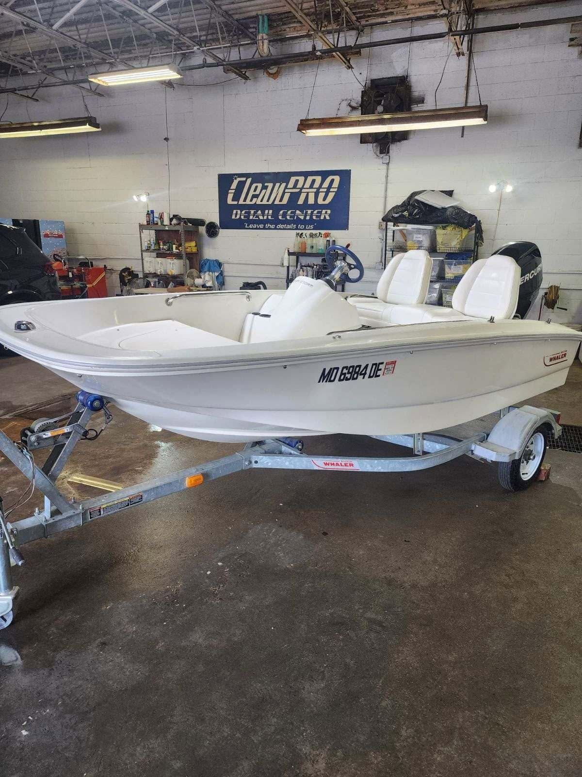 White boat on a trailer inside a workshop with a blue sign on the wall.