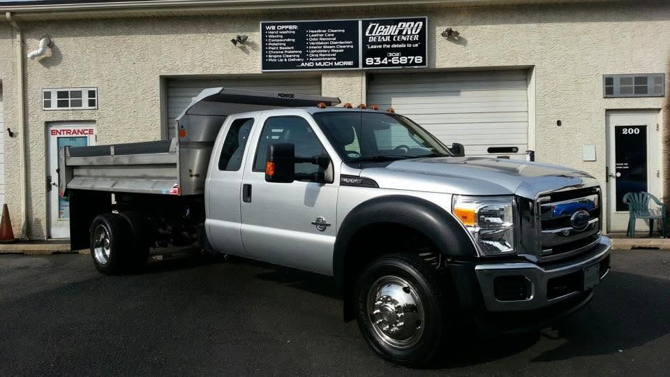 White and silver flatbed work truck parked outside a garage under signage.
