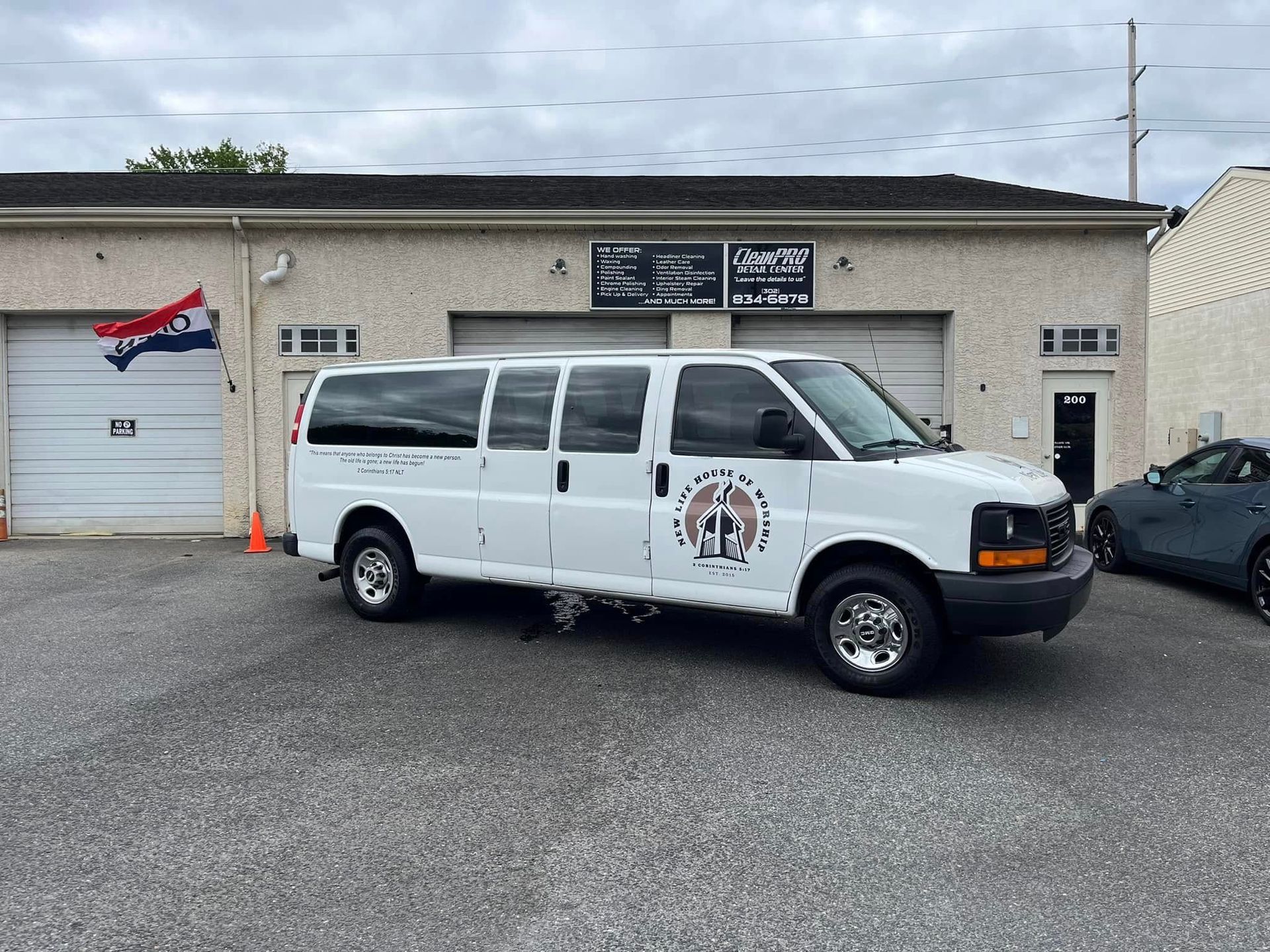 White van parked outside a small business building with a Canadian flag sign and a black car рядом
