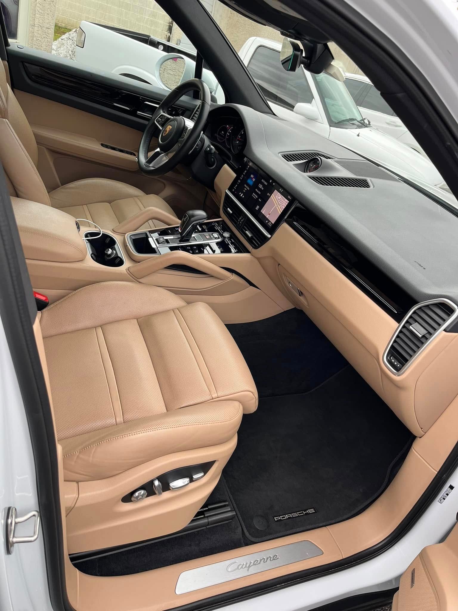 Luxury car interior with tan leather seats, black floor mats, and open driver door.