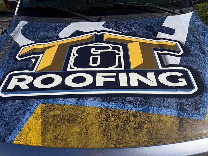 A truck hood wrap features a large T&T Roofing logo in yellow, white, and navy blue over a blue and yellow textured pattern.