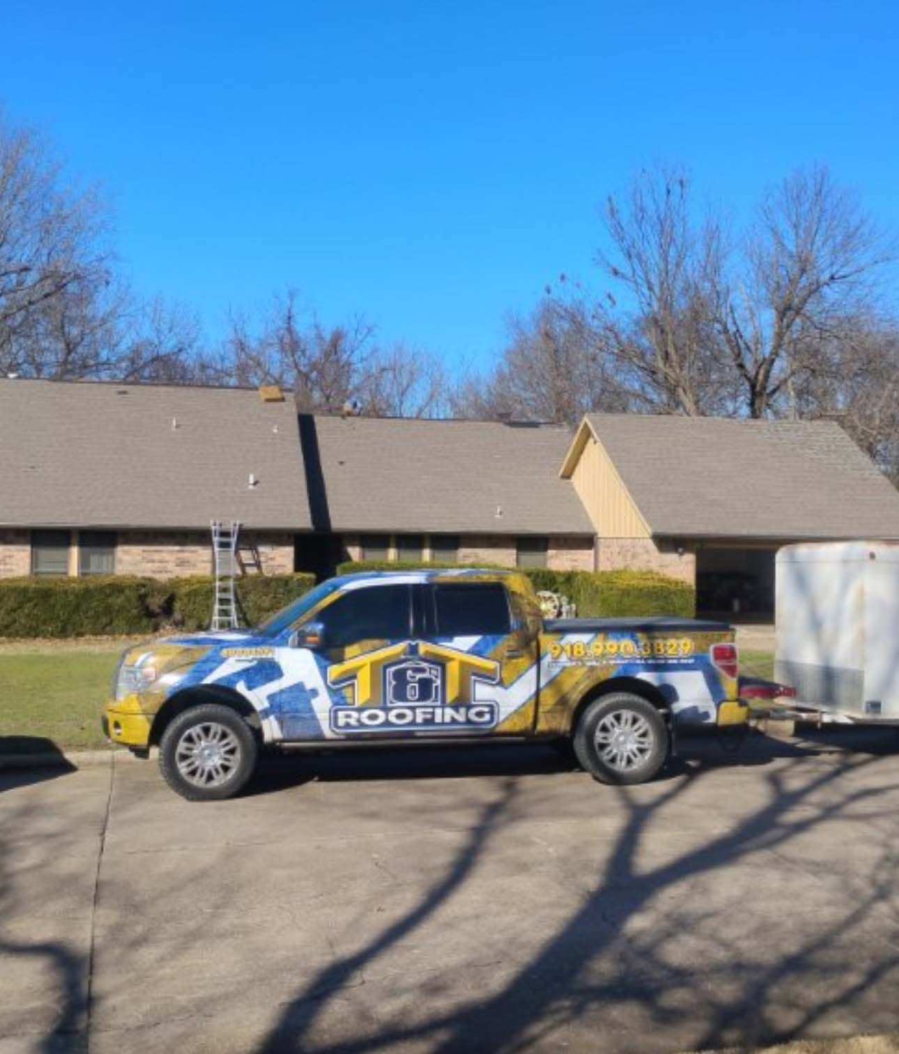 A branded roofing company pickup truck with a trailer parked in a residential driveway in front of a house.