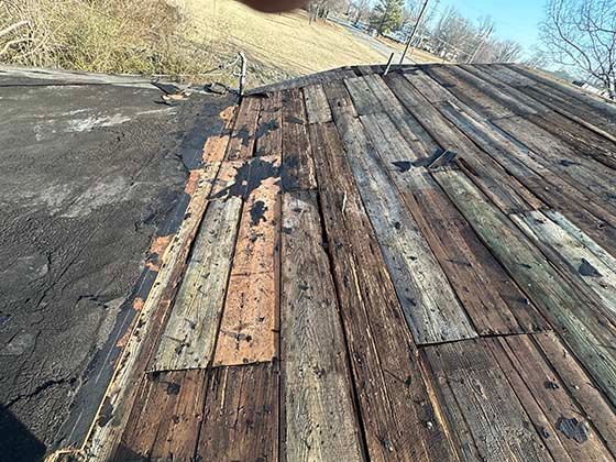 A weathered wooden roof deck with partially removed roofing material, showing boards and nails under an open sky.