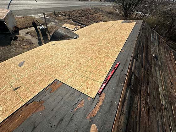 A partially re-roofed structure showing new OSB plywood panels installed next to worn, exposed wooden decking.