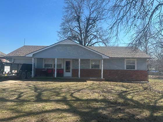 A one-story suburban home with a gable roof, light blue siding, and a red brick base, featuring a front porch and deck.