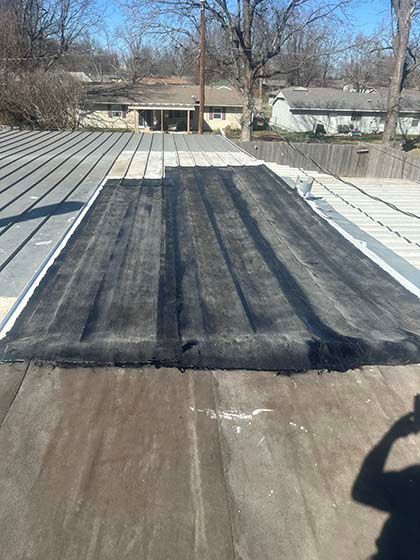 A view from a roof showing a patch of black roofing membrane being installed over worn, brown underlayment.