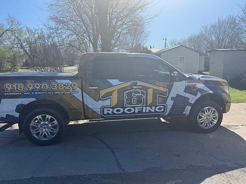 A black, white, and gold branded T&G Roofing pickup truck parked on pavement in an outdoor setting.