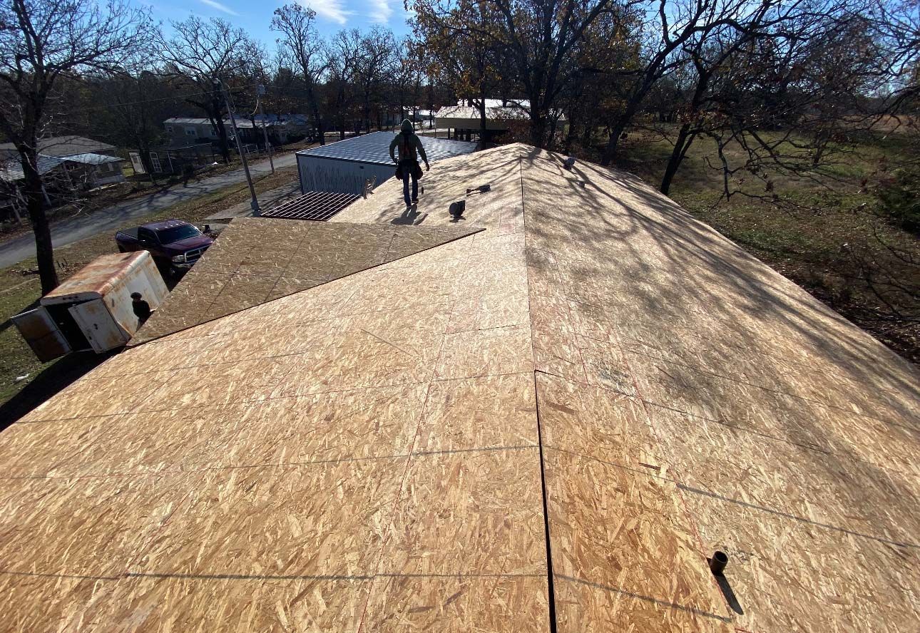 A worker walks across a newly installed plywood roof deck on a sunny day.