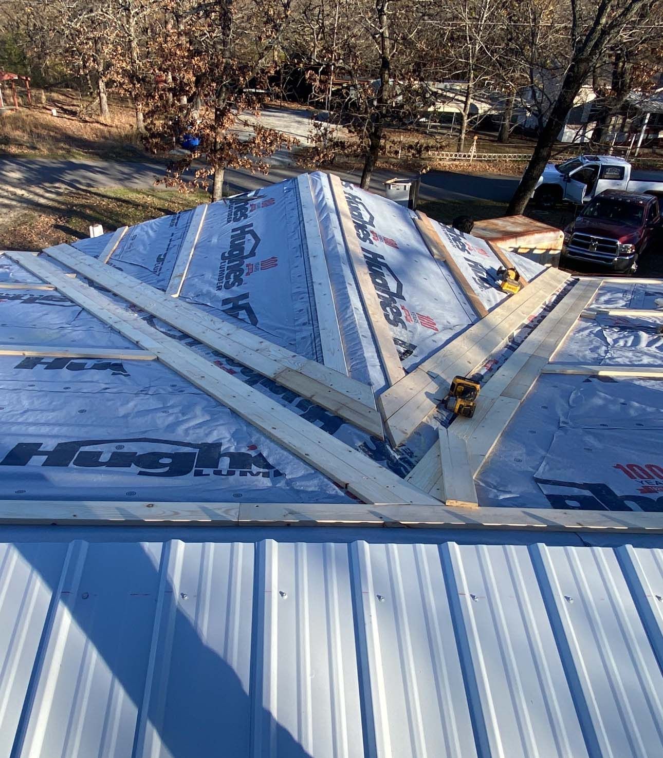 A residential roof under construction with light blue underlayment and wooden battens installed over metal panels.