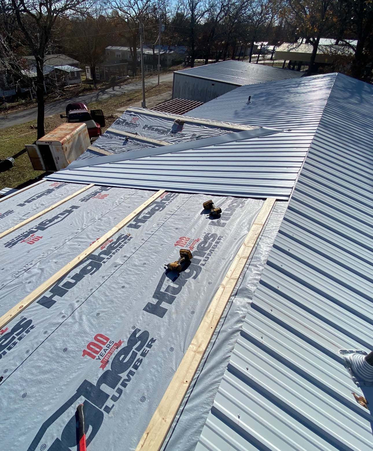 A partially installed metal roof over grey synthetic underlayment on wooden battens, with a suburban background.