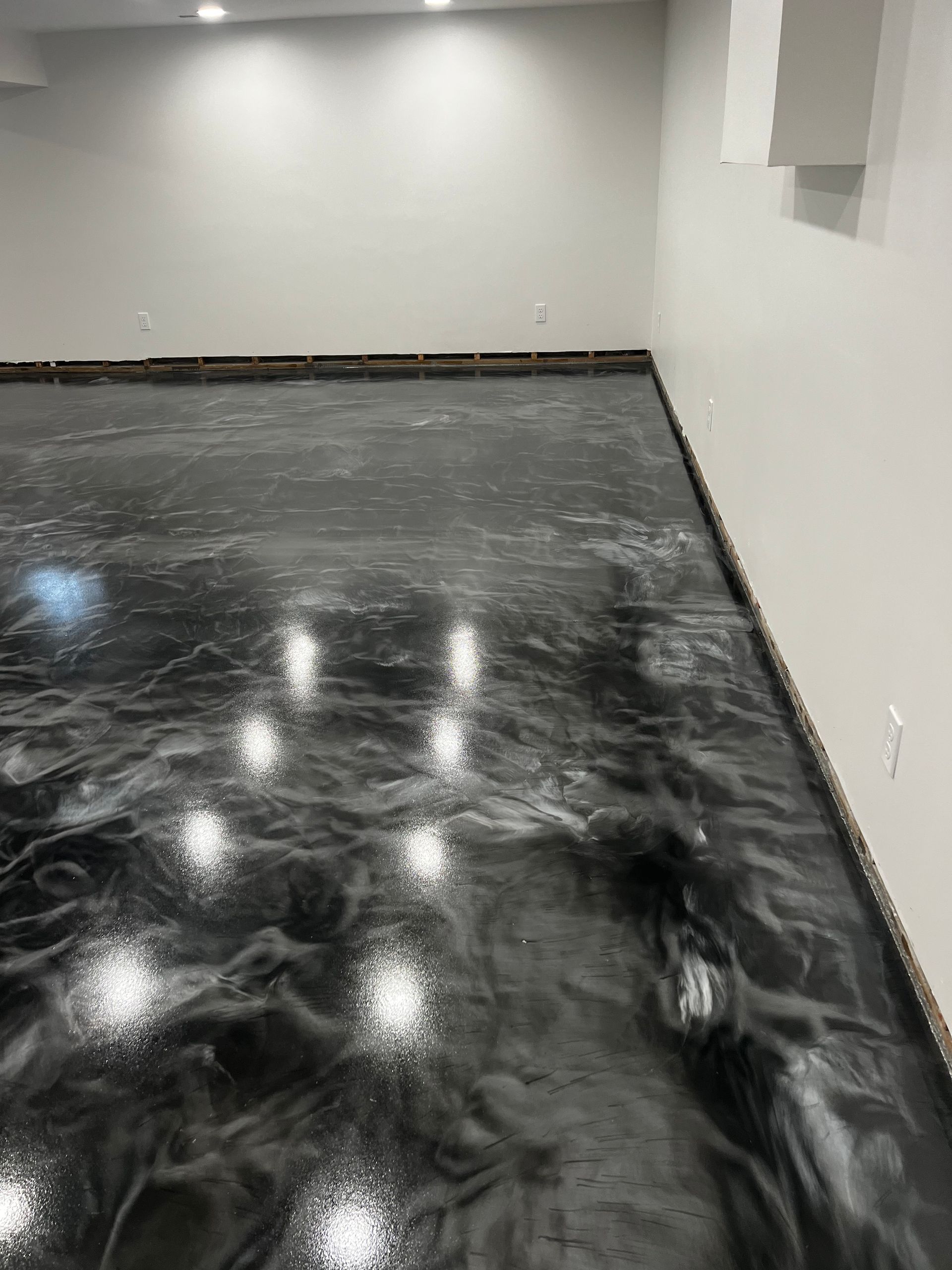 Glossy epoxy floor with swirling gray and black patterns, in a mostly empty white-walled room.