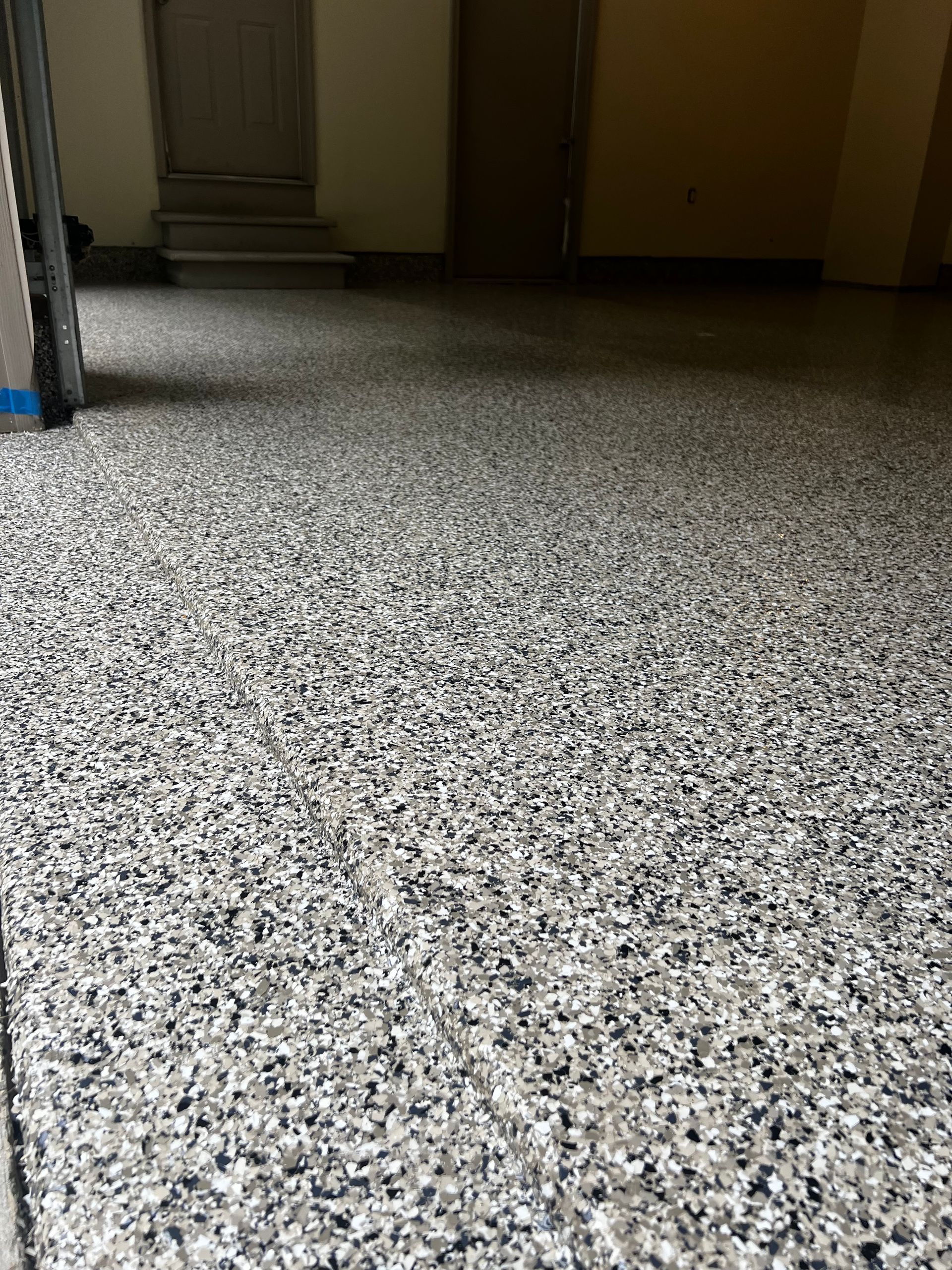 Speckled floor with gray, white, and black chips, in a garage setting with doors in the background.