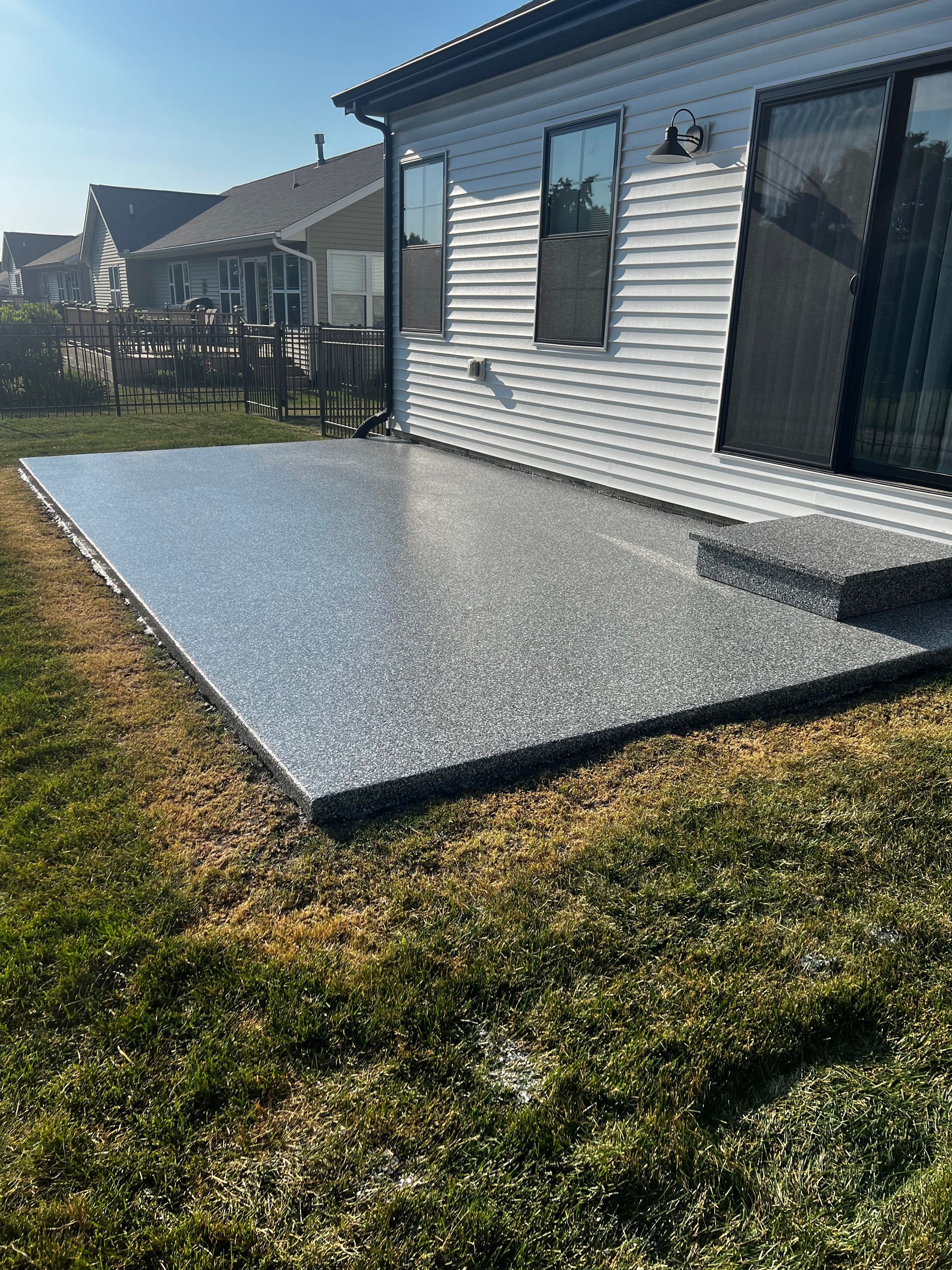 A concrete patio is sitting in the grass in front of a house.