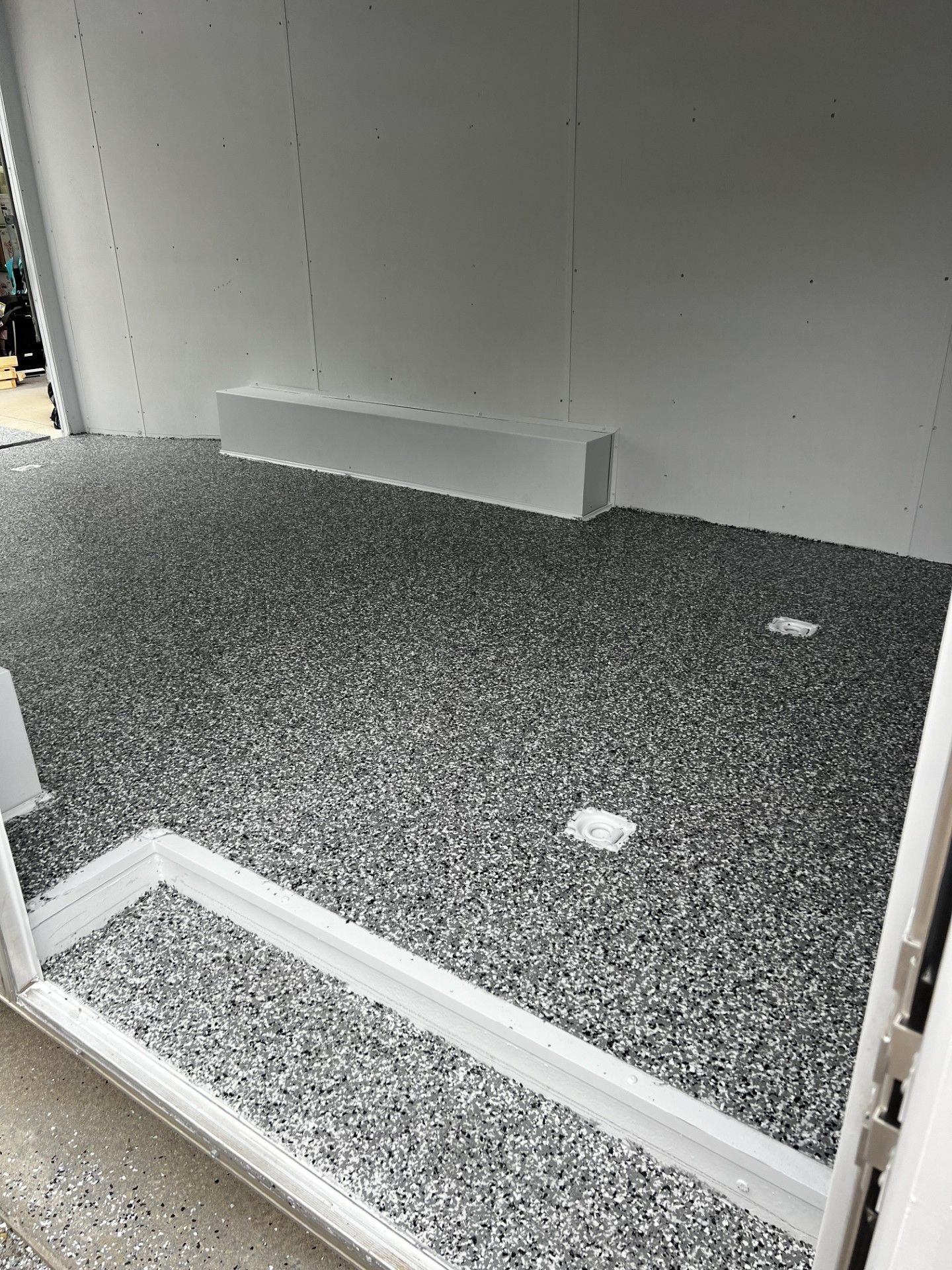 Inside of a trailer with a gray epoxy floor and white walls.