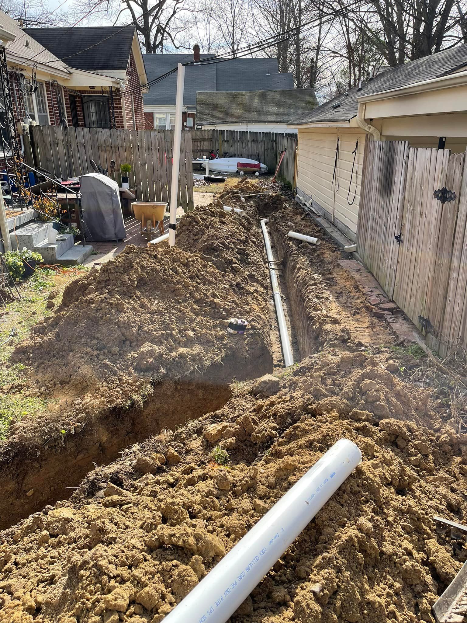 Backyard trench with exposed dirt, white PVC pipe, and garage walls on both sides