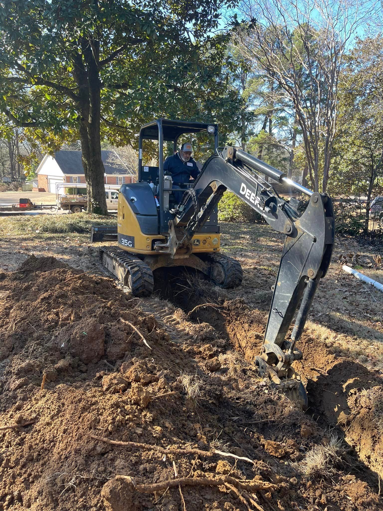 Mini excavator digging a trench through a wooded yard covered in autumn leaves.