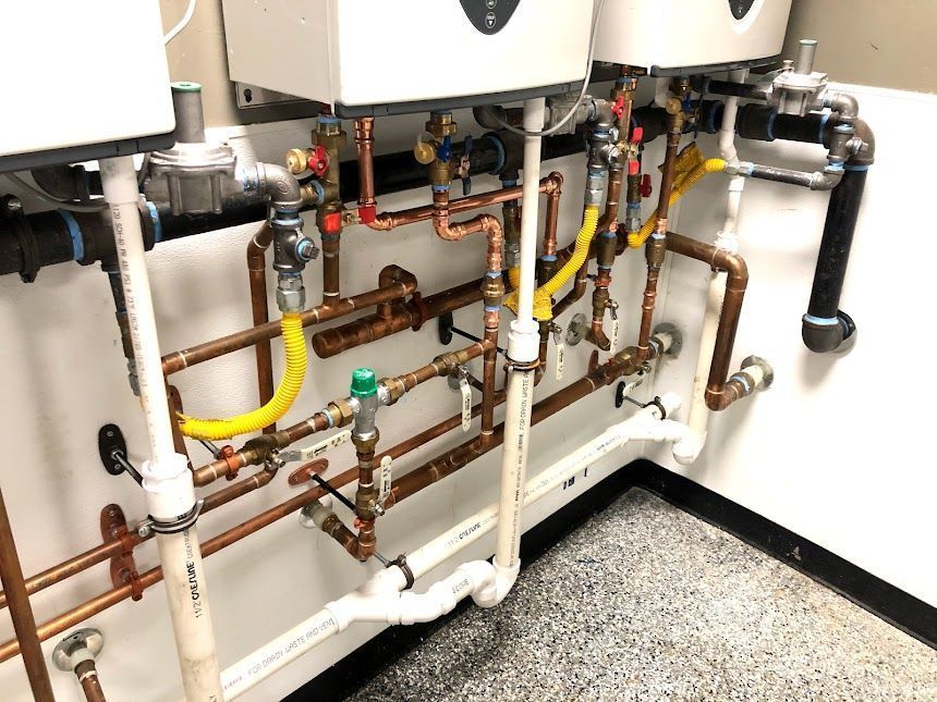 Industrial plumbing and pipes beneath equipment, with copper, white, and yellow tubing in a mechanical room