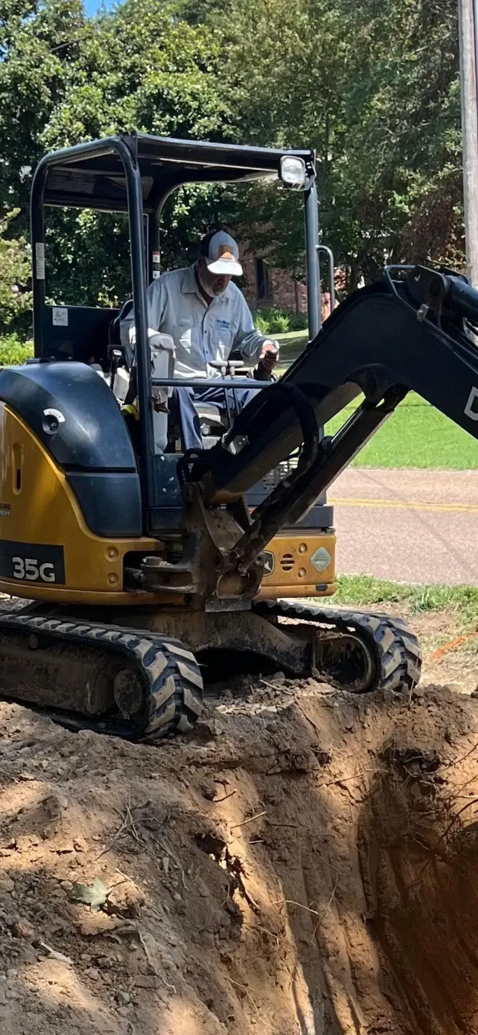 Yellow excavator digging a trench in a dirt field, with an operator in the cab.