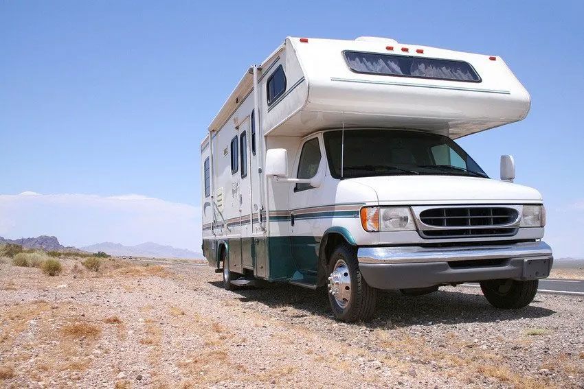 A white rv is parked on the side of a dirt road