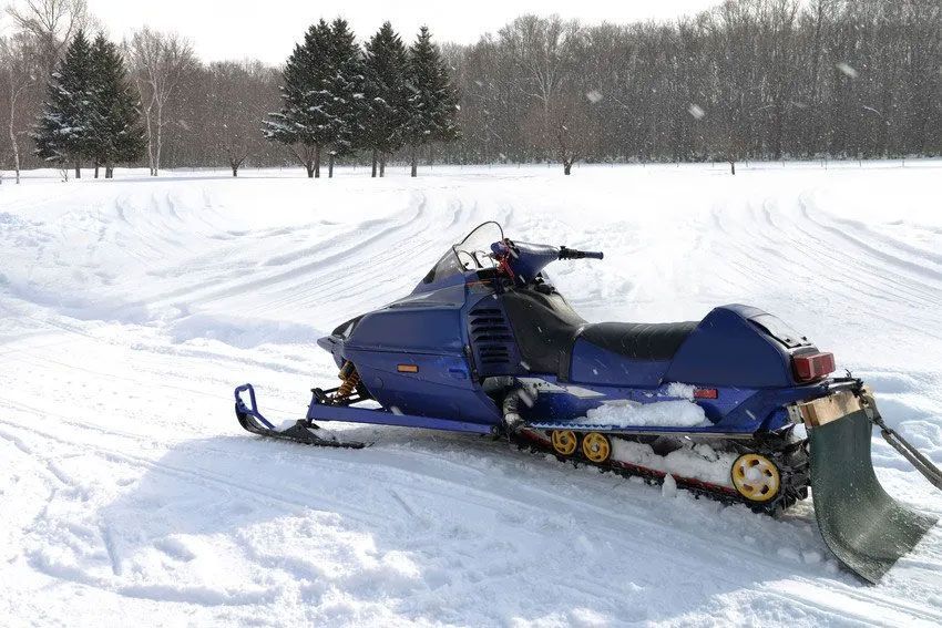A blue snowmobile is parked in a snowy field