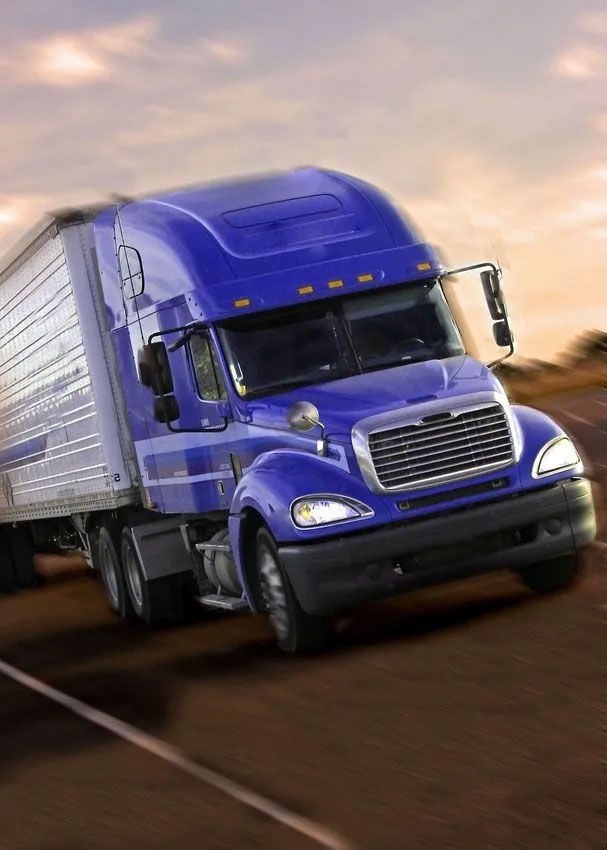 A blue semi truck is driving down a road.