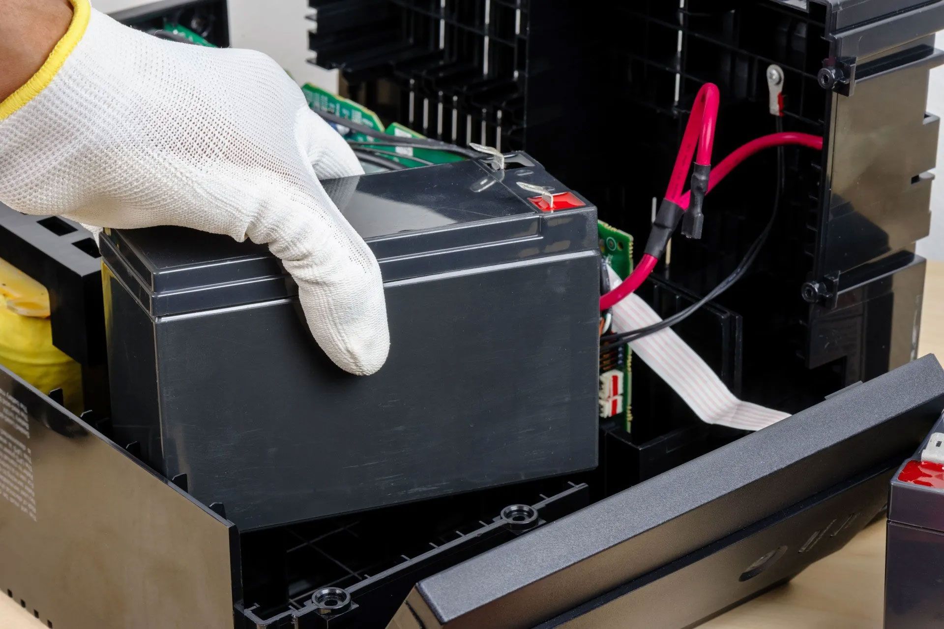 A person wearing gloves is holding a battery in their hand.