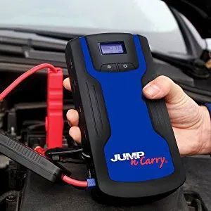 A person is holding a jump starter in their hand in front of a car.