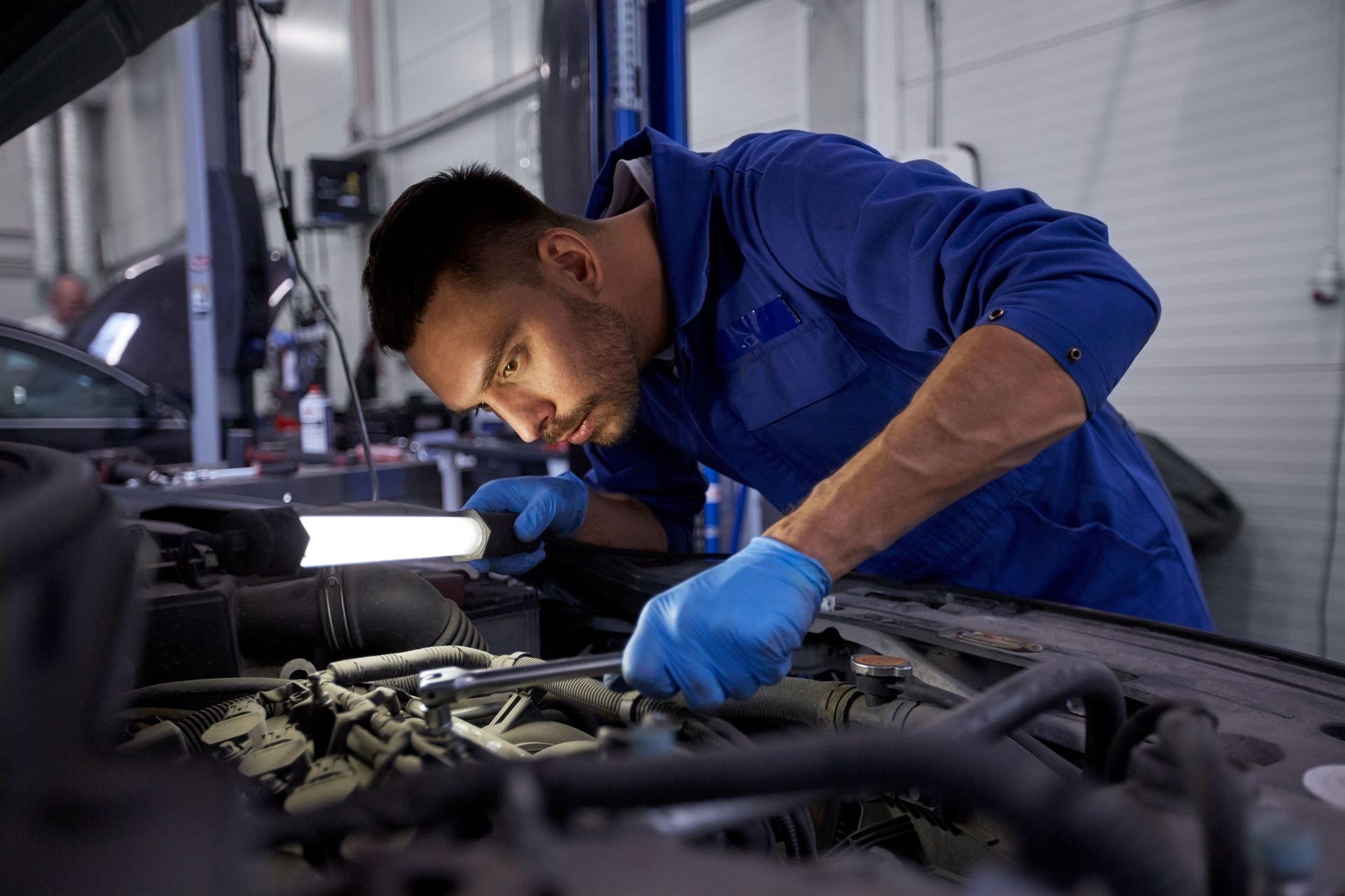 Mechanic in blue coveralls and gloves inspecting a car engine in a garage