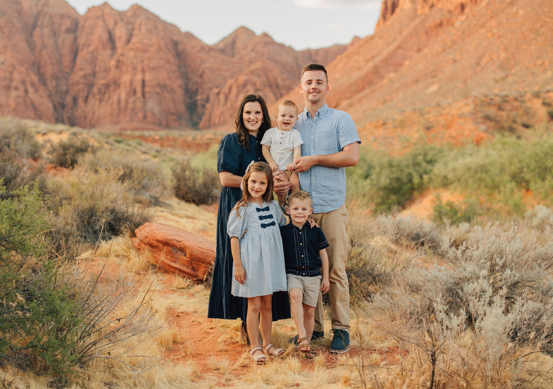 Family of four posing on a desert trail with red rocky mountains in the background