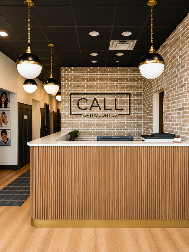 Reception desk in a modern office lobby with wood slat front, brick wall, and hanging globe lights.