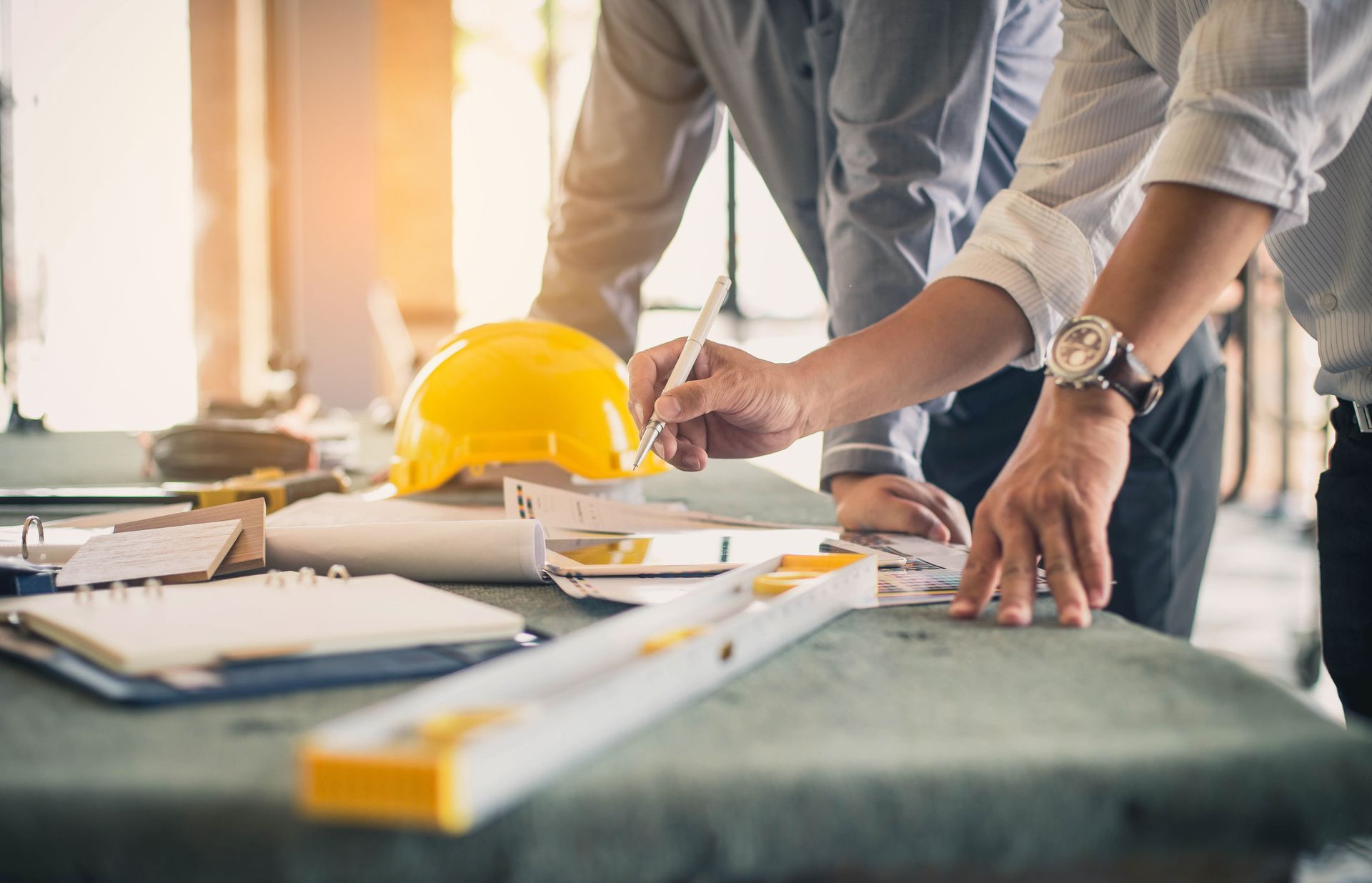 Two people reviewing blueprints at a table with a yellow hard hat and level.