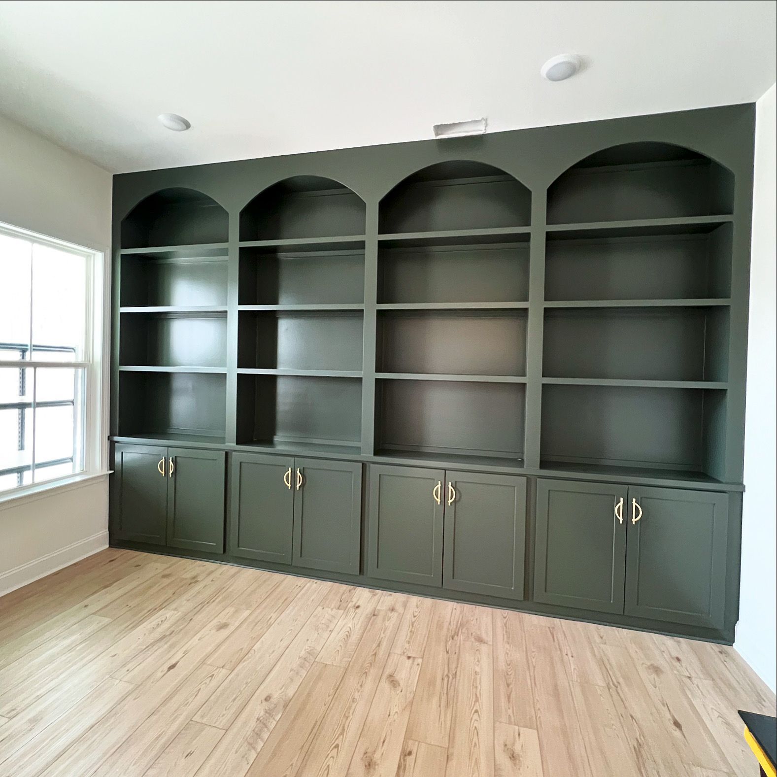 Dark gray built-in shelving with cabinets in a bright room with hardwood floors and a window