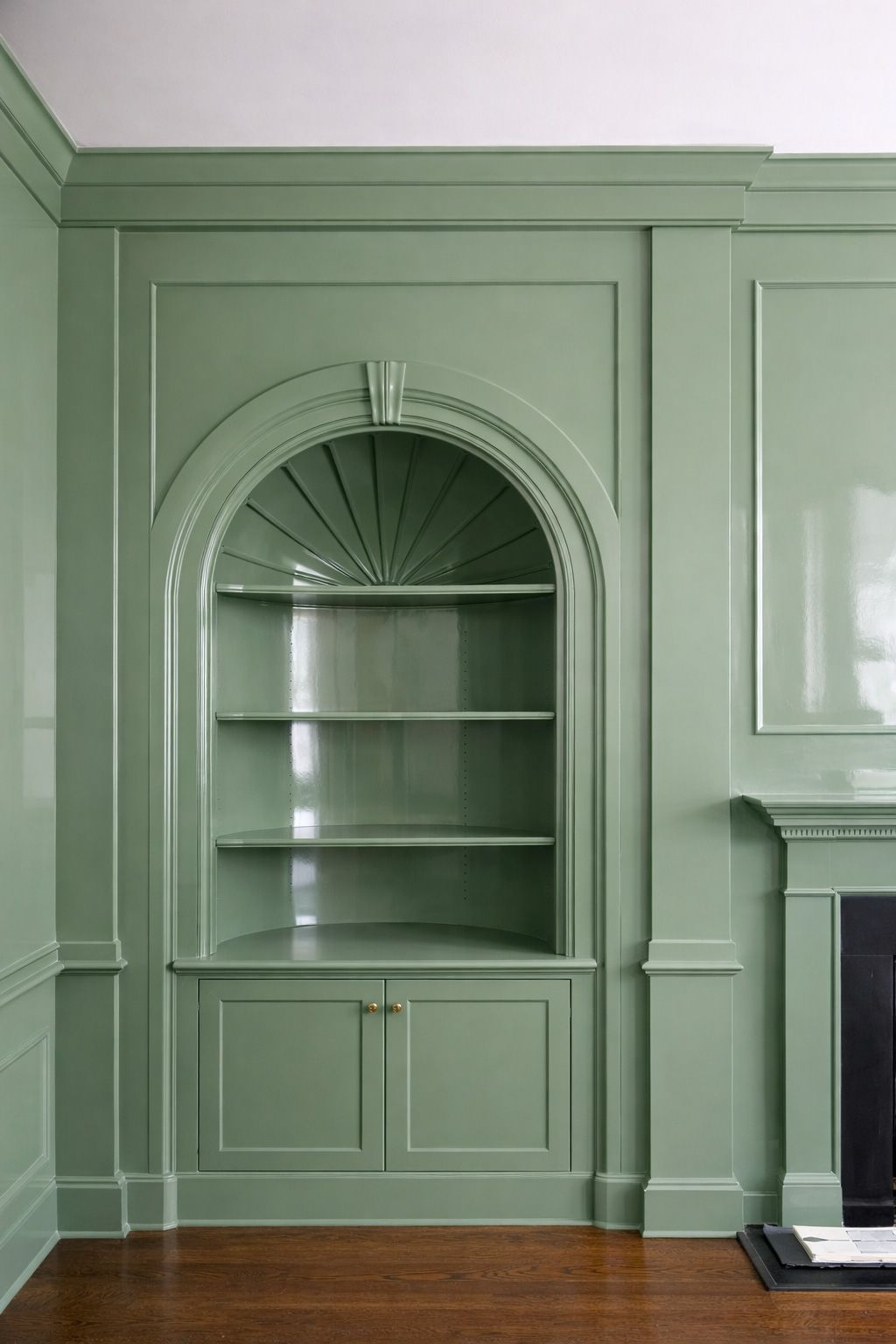 Built-in sage green arched shelving beside a fireplace in a paneled room