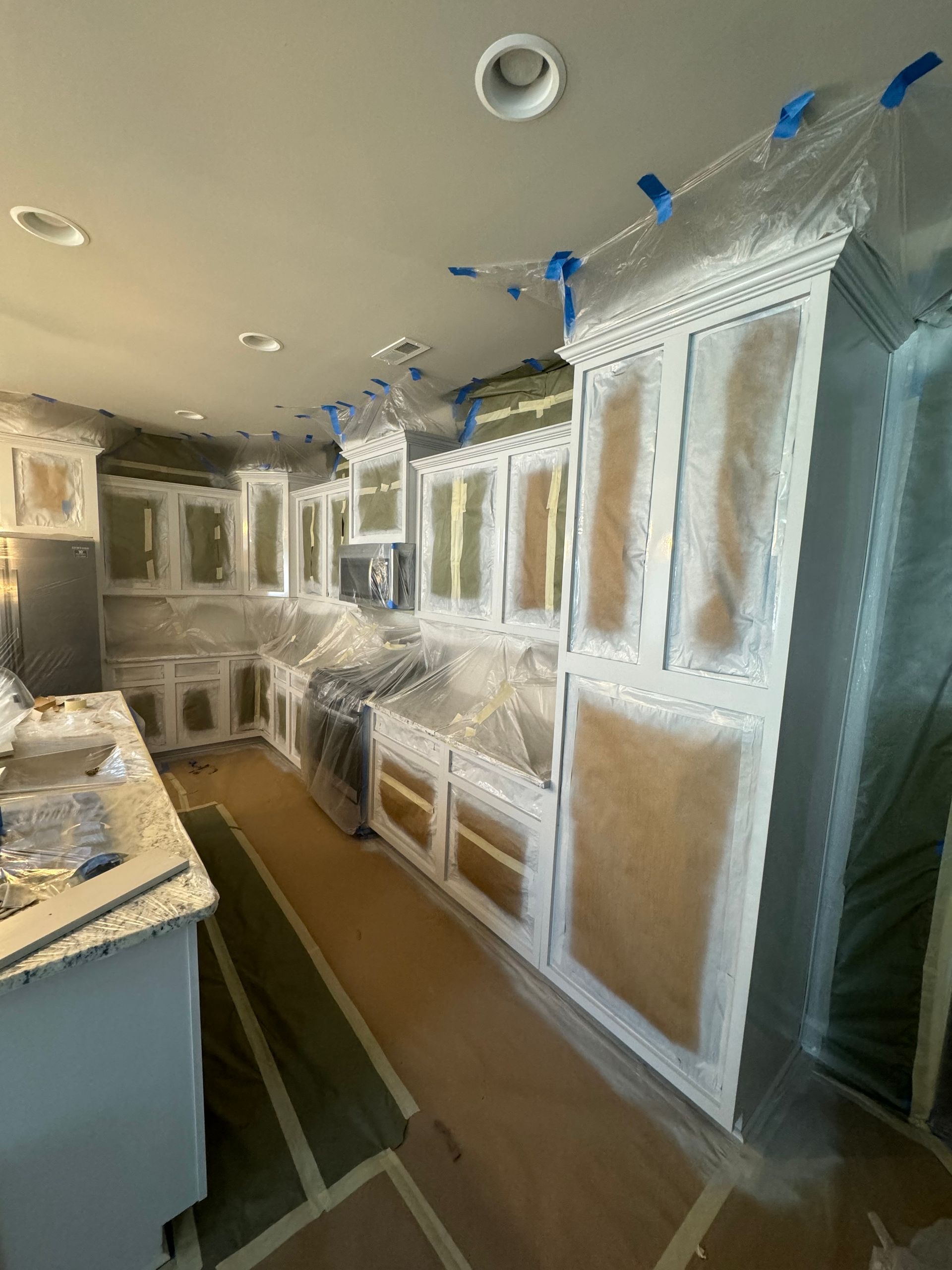 Kitchen cabinets wrapped in plastic sheeting during renovation, with countertops and walls unfinished