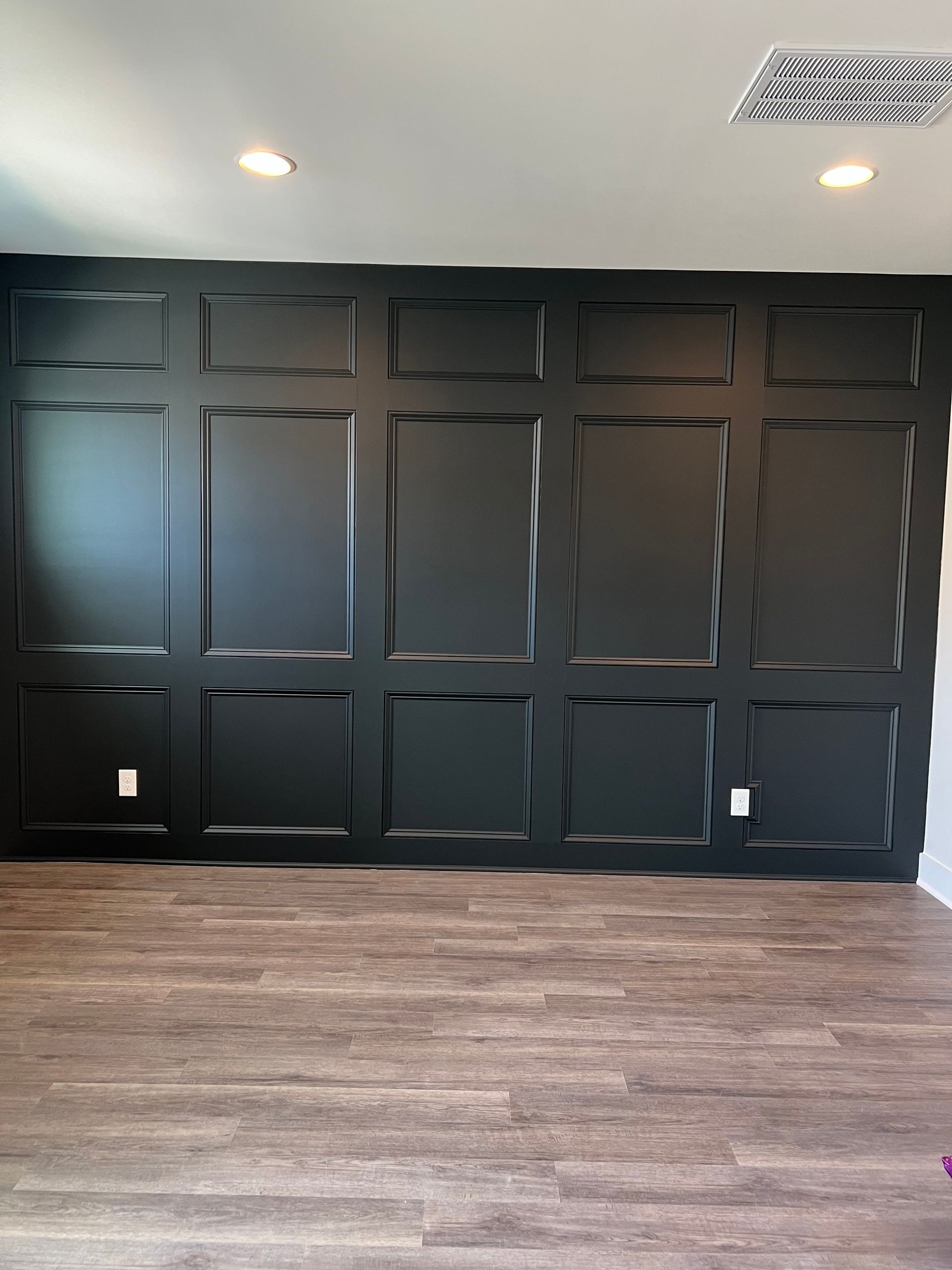 Empty room with black paneled accent wall, light wood floor, and recessed ceiling lights.