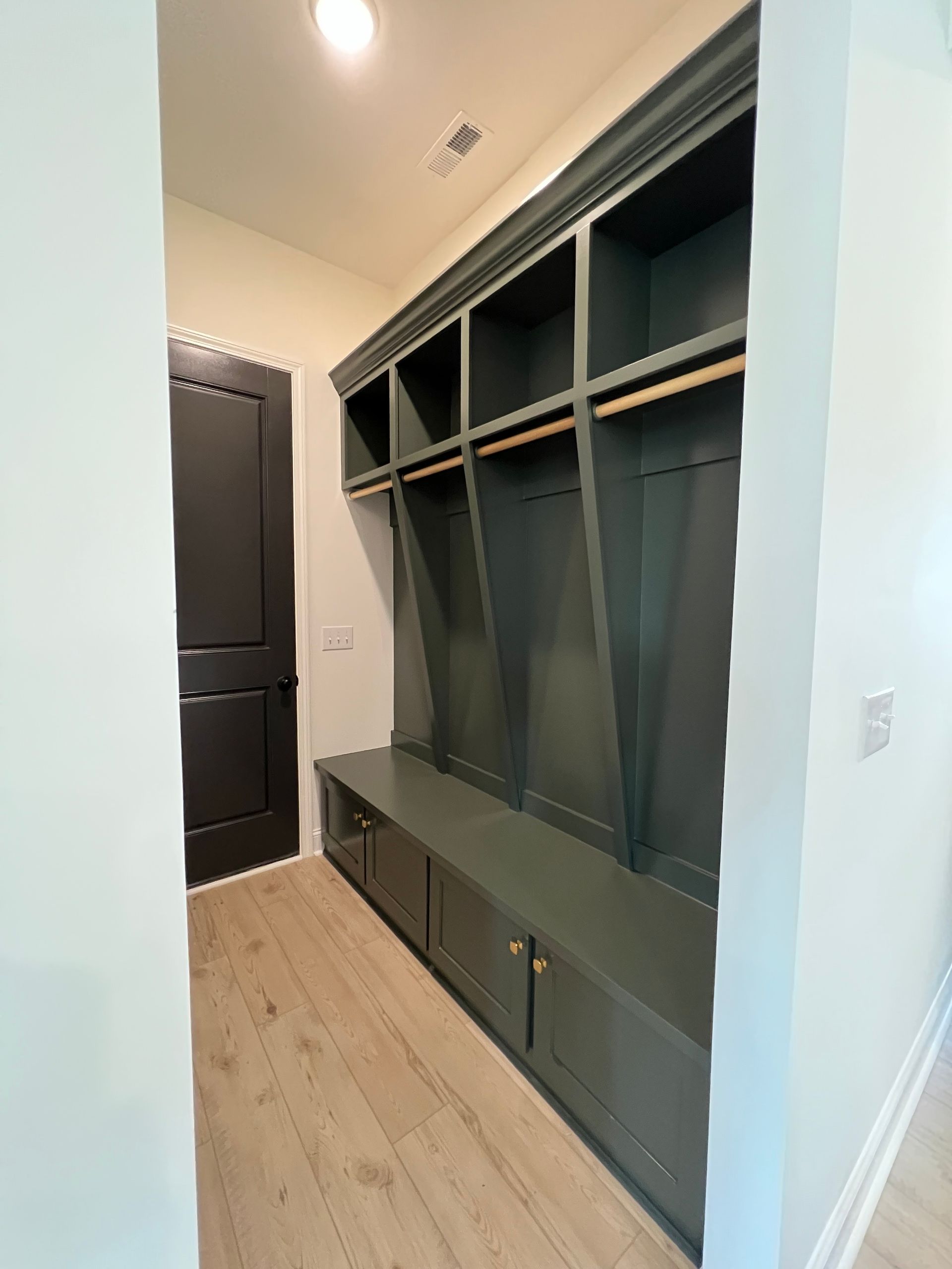 Modern entryway with built-in dark green storage cubbies and bench along a light wood floor
