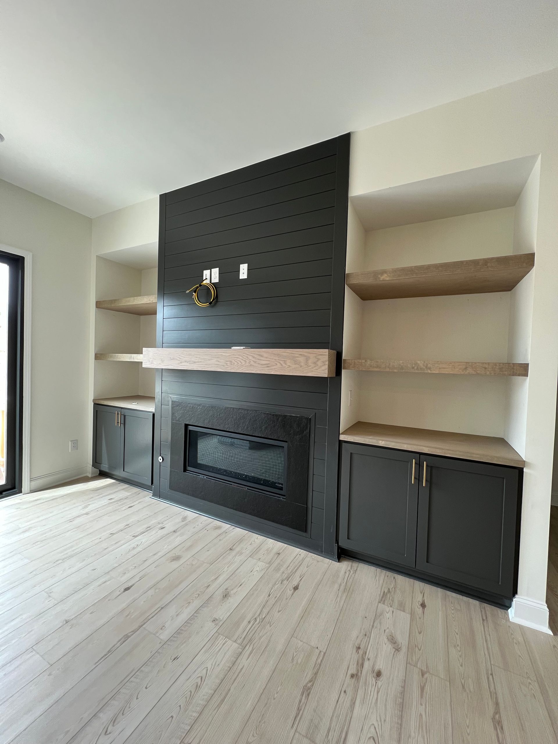 Modern living room fireplace wall with black brick, open shelves, and built-in cabinets