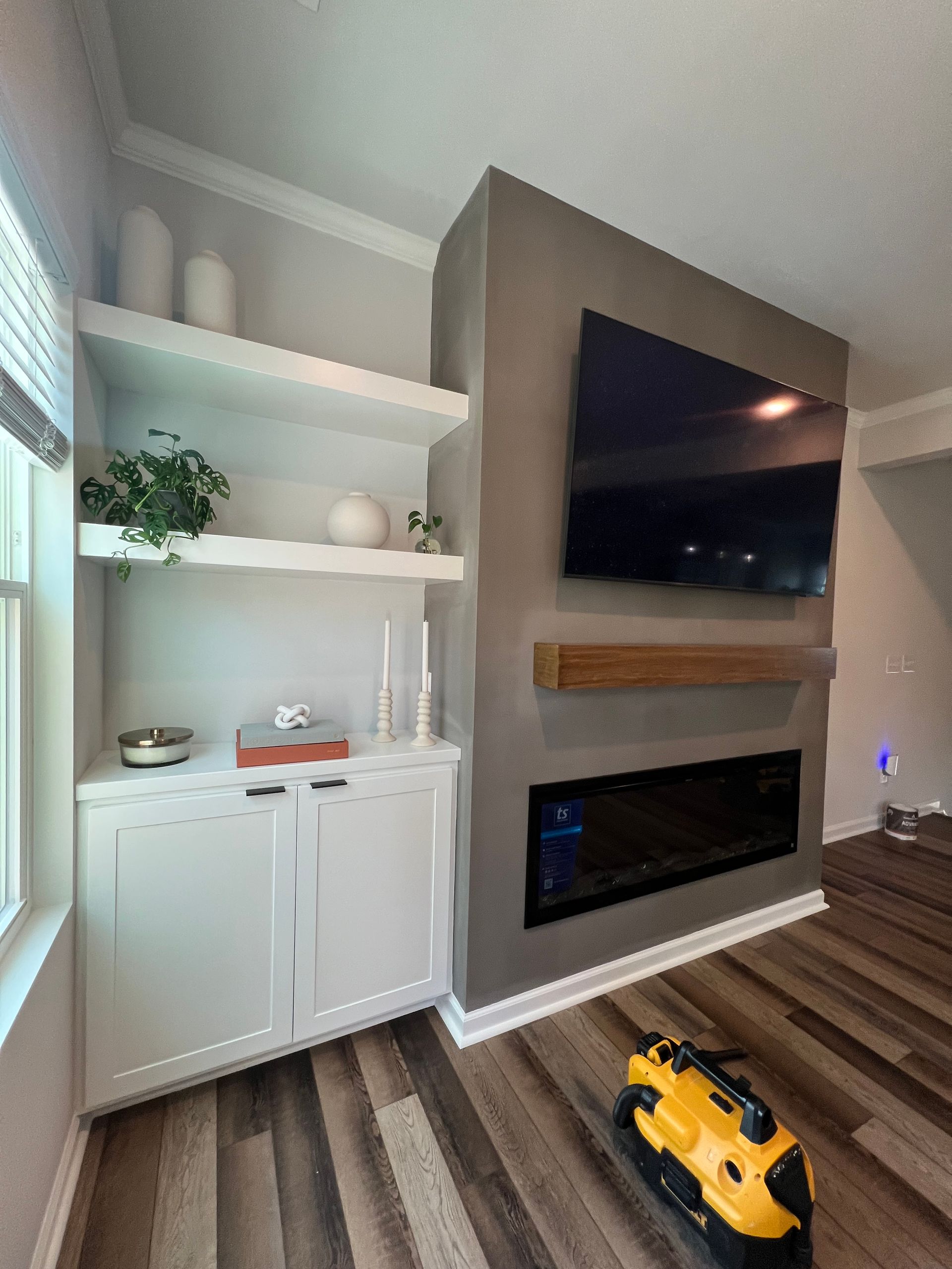 Modern living room corner with white shelves, wall-mounted TV over a fireplace, and a yellow toy truck on hardwood floor