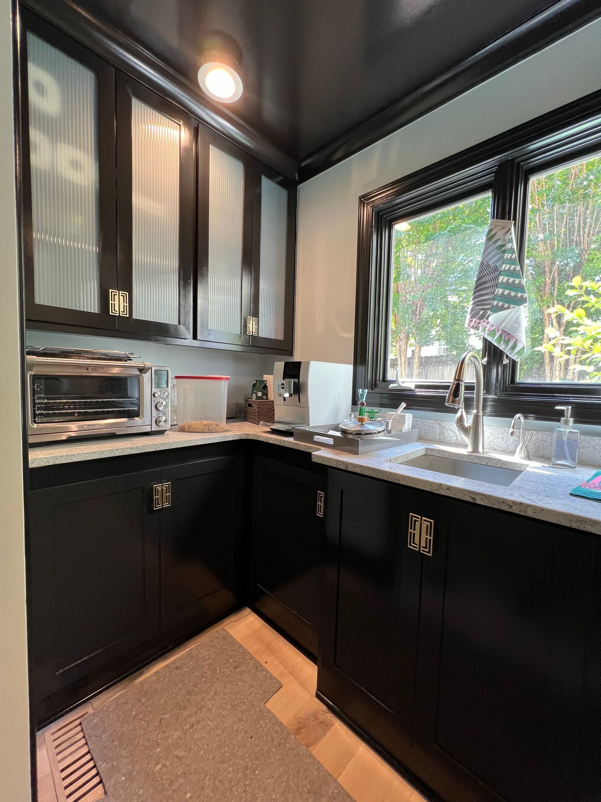 Compact black kitchen with glossy cabinets, stainless appliances, and a sink by a bright window.