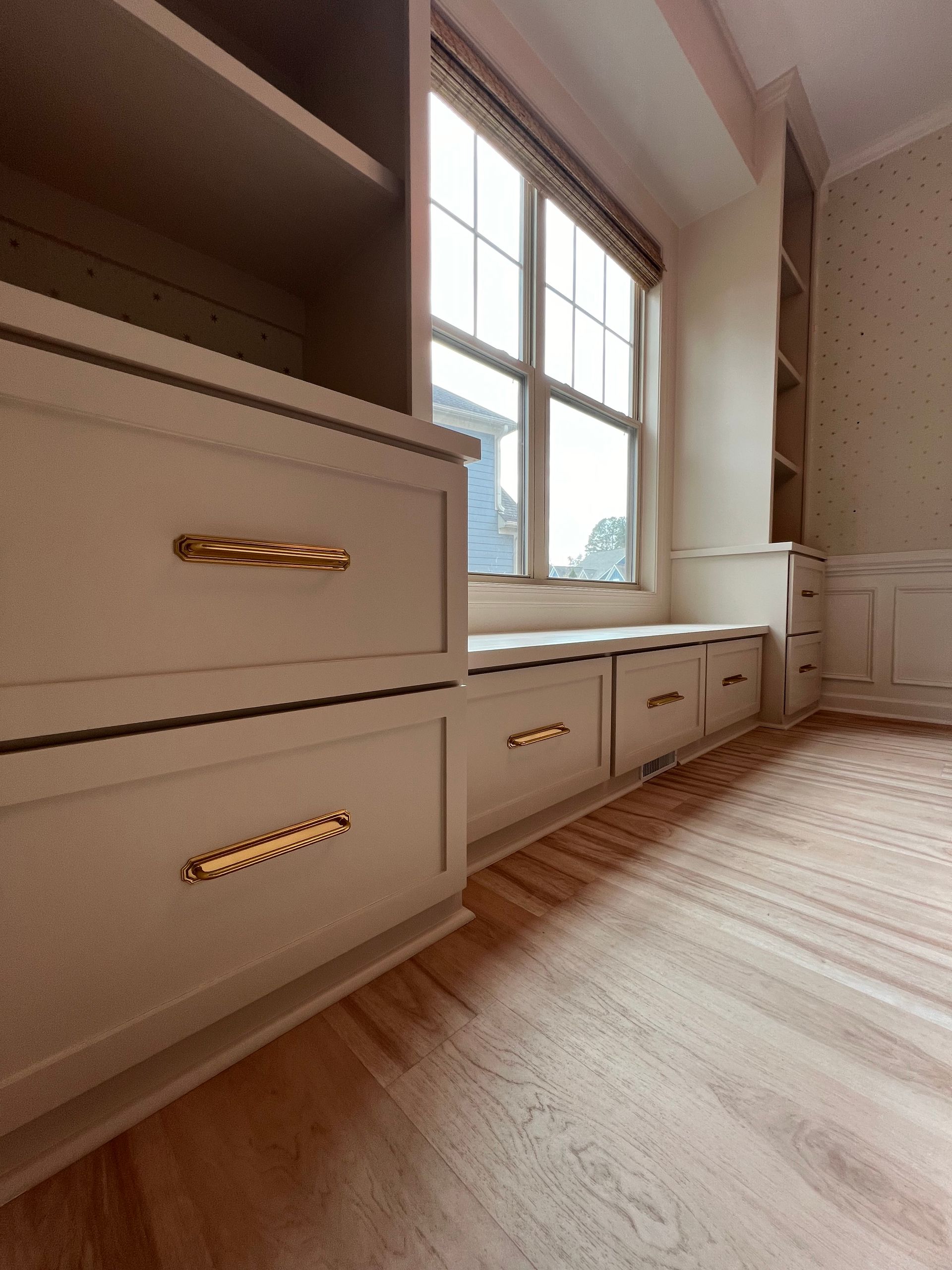 Built-in white cabinets and drawers beneath a large window in a bright room
