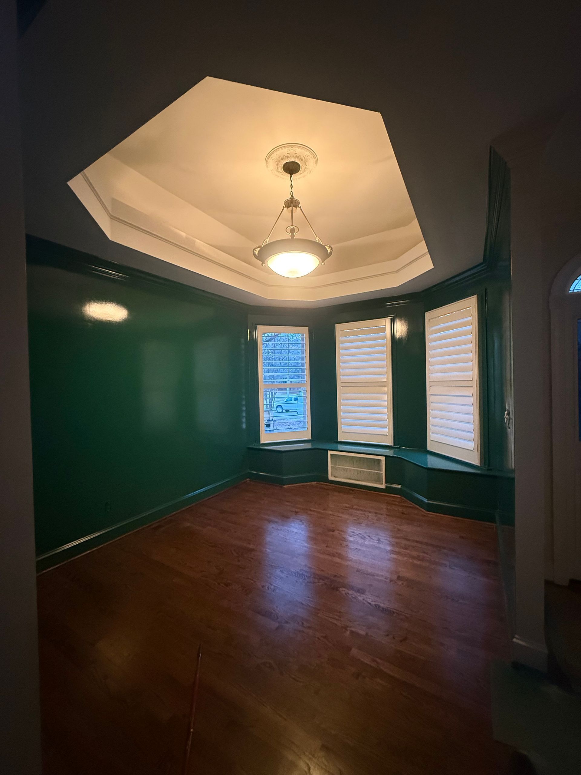 Empty room with dark green walls, hardwood floor, octagonal ceiling, and bay windows with a radiator.