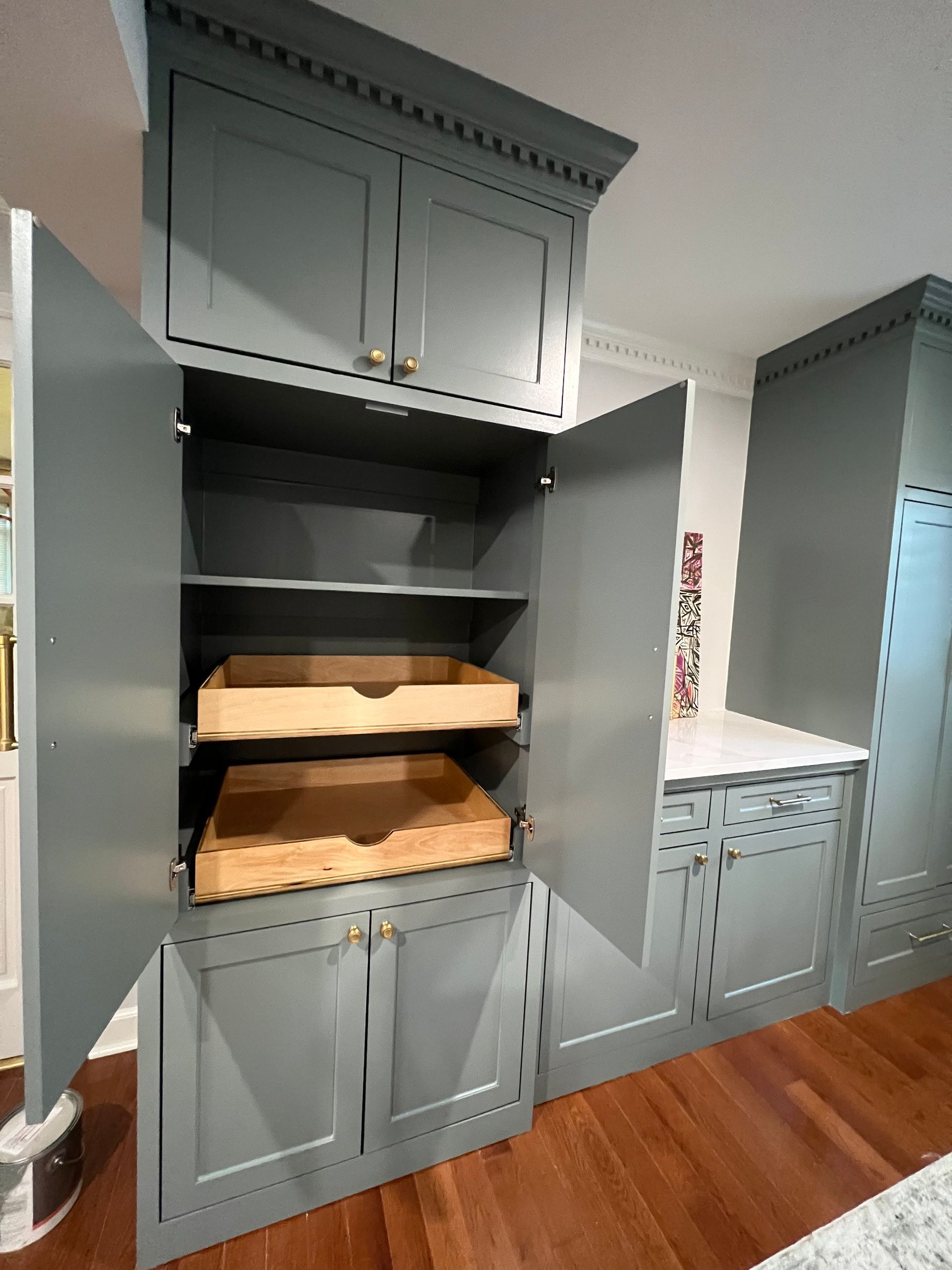 Gray built-in kitchen cabinets with open shelving and woven baskets beside a pantry nook.