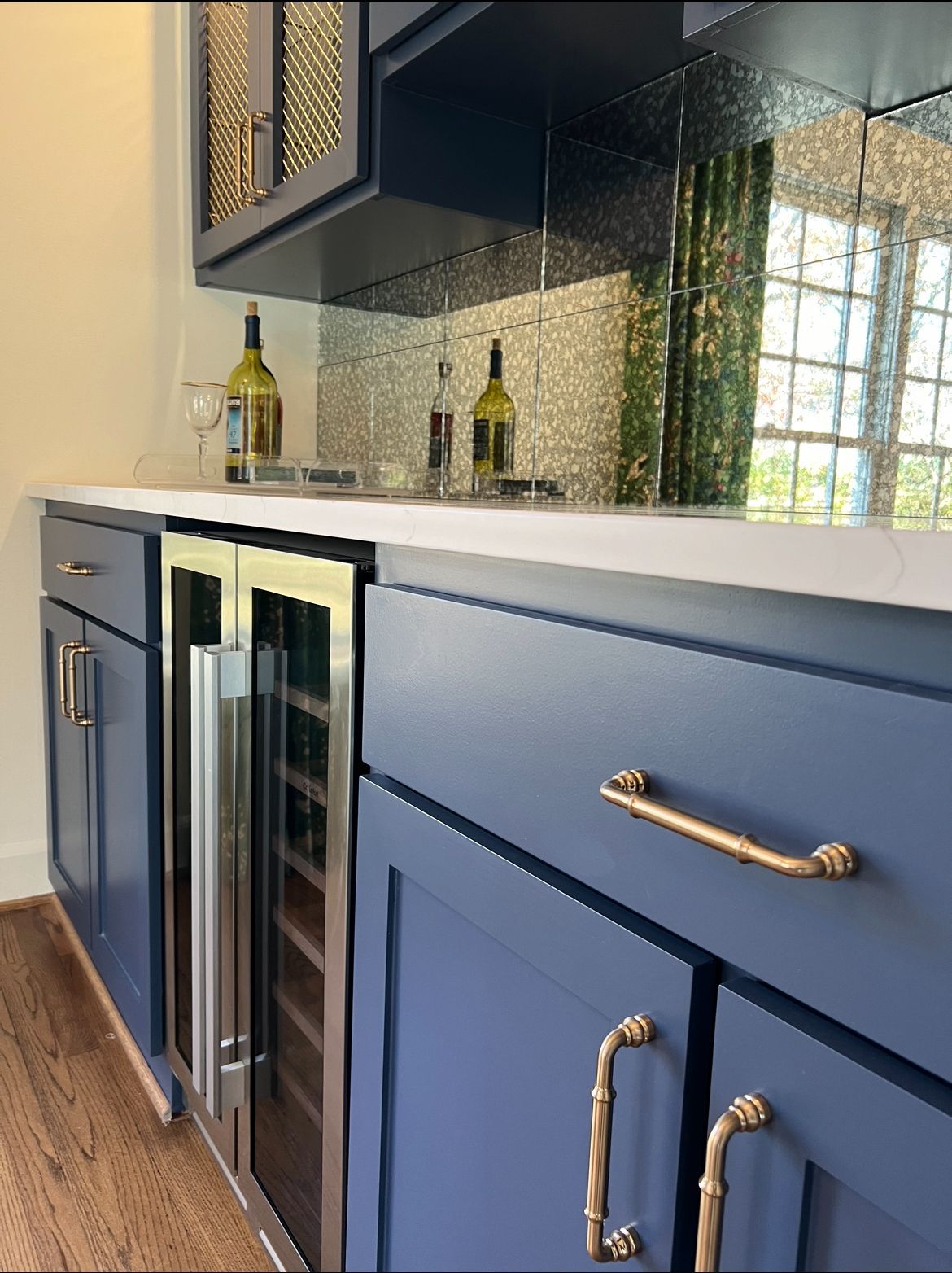 Modern kitchen with navy cabinets, white countertop, gold hardware, and mirrored backsplash