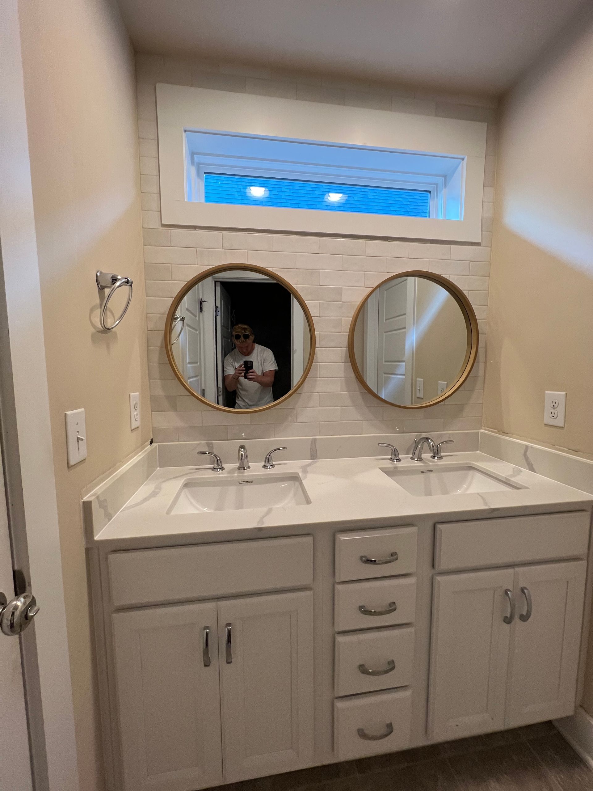 Small bathroom vanity with double sinks, two round mirrors, and a narrow window above.